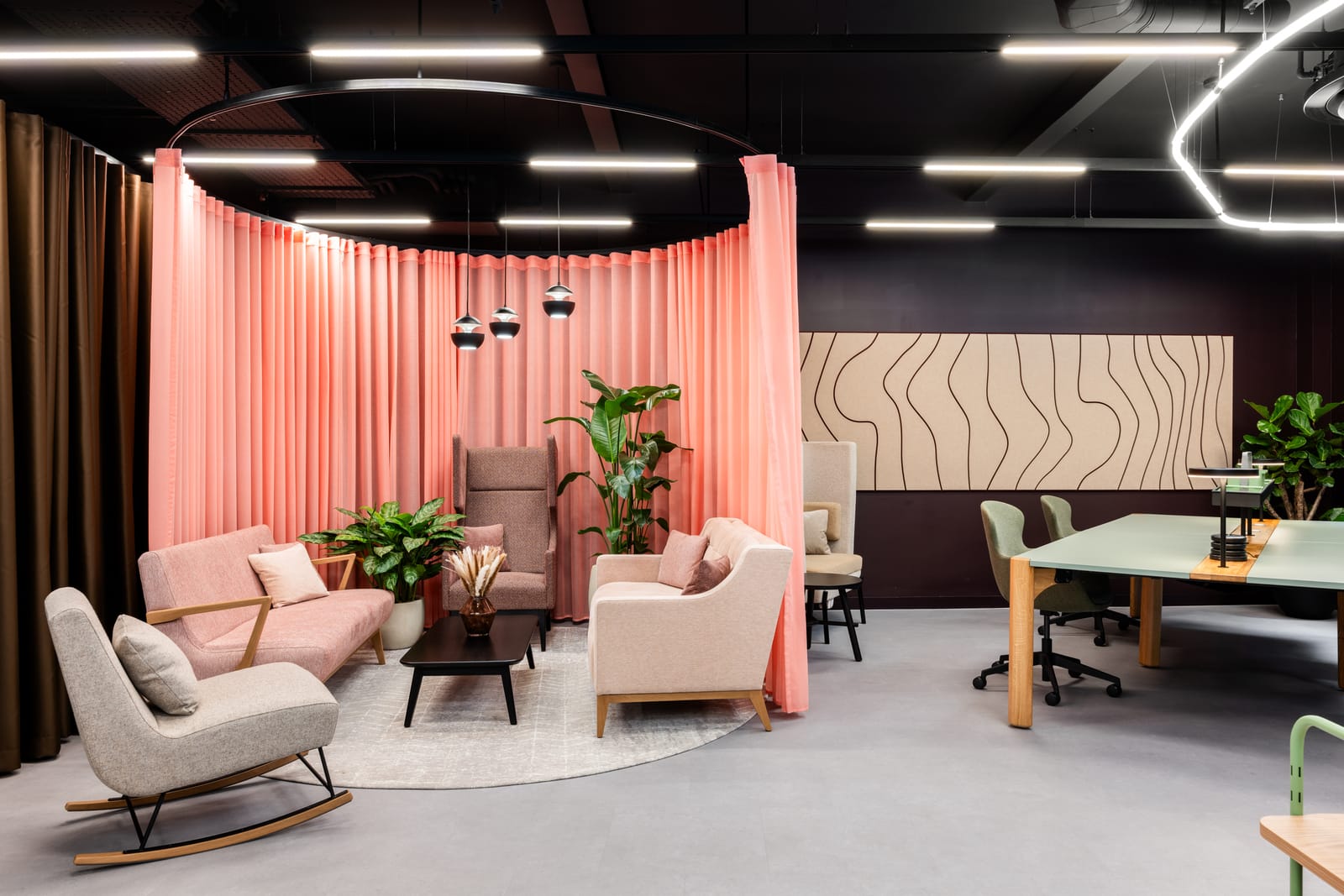 Curtained finishes area with blush armchairs, a meeting table and a wavy acoustic feature wall