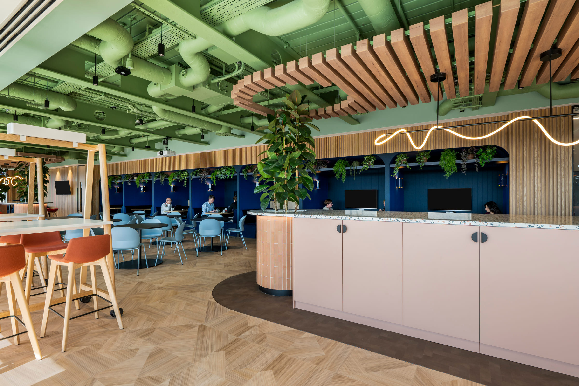 The Culture Hub on Floor 7 with pink tiled island, terrazzo top, large plant and blue back wall