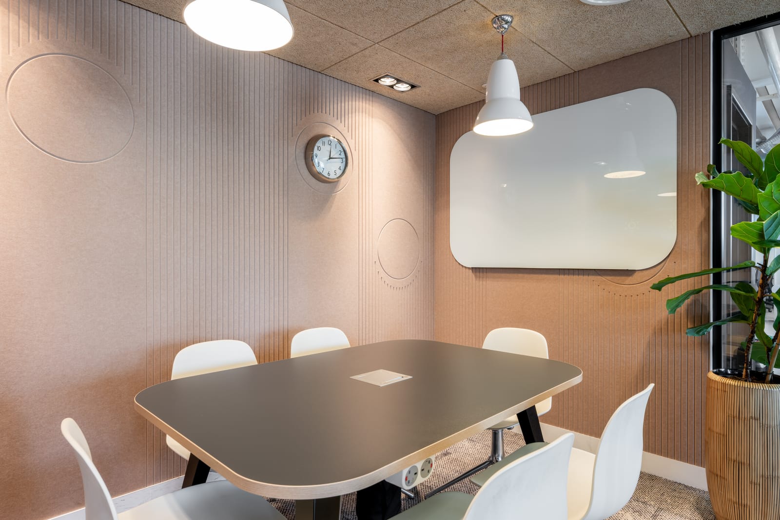 Meeting room lined with blush acoustic felt, a rounded whiteboard and soft white chairs
