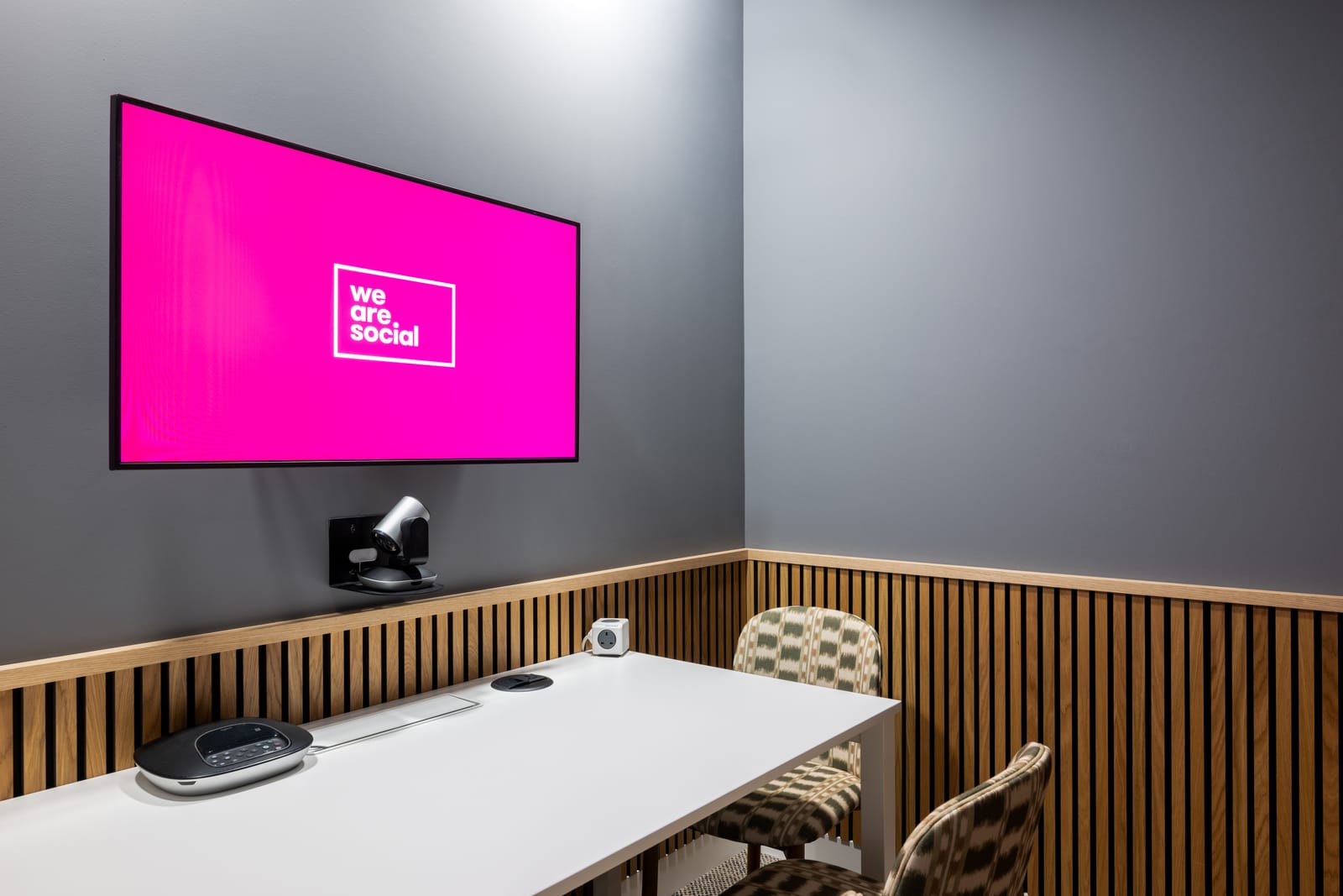 Video call booth with a white worktop, patterned chairs and the We Are Social logo on screen