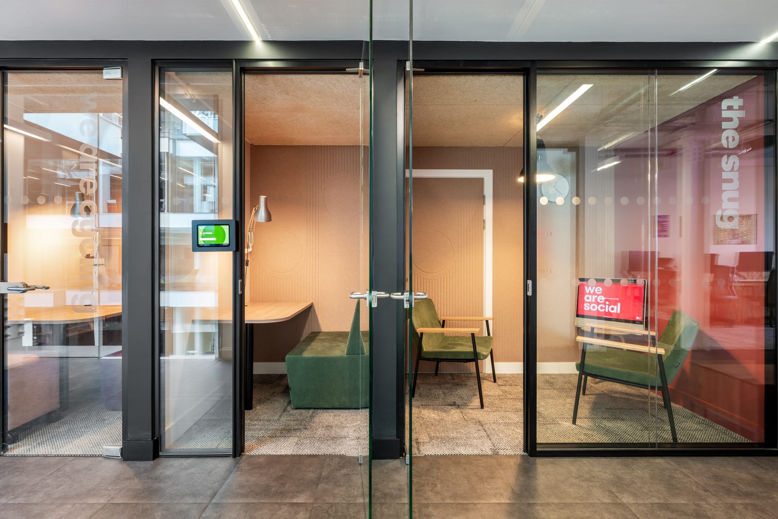 The snug, a glazed lounge room with green velvet armchairs and a We Are Social screen